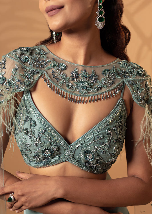 Woman wearing a intricately designed green blouse with embroidery and embellishments.